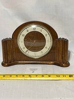 Full front view showing the wooden Art Deco case, clock face and base next to a measuring tape indicating about 12 inches wide.