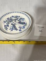 Stack of eight ceramic saucers with floral and woman design on white background showing size measurement