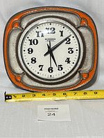 Front view of clock on white backdrop with measuring tape at base