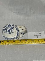 Front side view of the white ceramic cat figurine decorated with blue floral patterns and gold accents. Measuring tape indicates approx 6.5 inches in length.