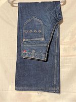 Folded denim jeans with star embroidery and red brand patch on pocket.