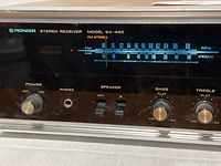 Close-up of front left side showing power knob, headphones jack, speaker selector switches, bass and treble knobs and FM/AM frequency display.