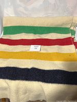 Blanket showing full width with distinct green, red, yellow, and navy stripes on a cream wool base.