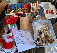 Photo showing six ping pong rackets, assorted sea shells in a container, two glasses, a white mug, small Canadian flag tray, two Christmas stockings, a vintage book, and assorted pens and pencils on a table.