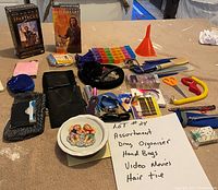Photo showing a variety of items including two VHS tapes, pill organizer, hair ties, scissors, cosmetic and personal items, small tools, and handbags.