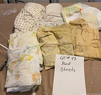 Photo showing nine assorted bed sheets including floral, checkered, and patterned designs arranged on a flat surface with a label indicating 'Lot # 47 Bed Sheets'.