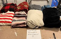 Photo of eight assorted blankets in various colors and patterns arranged on a surface with a handwritten sign reading 'Lot #35 Blankets Assortment 8'.