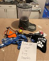 Photo showing multiple cat and dog supplies including pet feeder, collars, harnesses, clothing, and accessories.