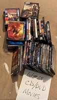 Photo displaying approximately 29 DVD movies stacked and spread on a carpeted floor. Titles visible include Spider-Man, Cars, and The Crusades among others.