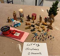 Full display of Christmas ornaments including nativity figures, miniature tree, candles, and ribbons on a table.