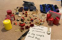 Photo showing the assortment of Christmas ornaments, leg weights, handbags, and candles arranged on the floor with a handwritten sign listing lot contents.