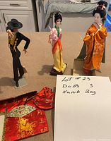 Photo showing three dolls and one red handbag placed on surface with handwritten note describing lot contents.