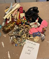 Photo showing a mix of jewelry including necklaces, bracelets, rings, two clown figurines, small vintage chest, pink slippers, cloth-wrapped hangers, and some collectible dice and pins.