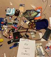 Overview of all items in the lot spread on a surface, showing mixed jewelry, fans, craft supplies and personal care items.