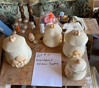 Photo of assorted kitchen supplies on a wooden table displaying four ceramic pumpkin-themed canisters, three wooden mills, four glass shakers, soap dispensers, and various utensils and kitchen items.