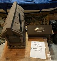 Photo showing two mail boxes side by side on a table with a note describing them as a roadside mail box and a house wall mail box.