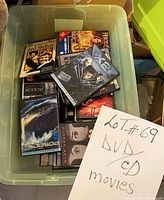 Plastic bin containing mixed DVD and CD movie cases with visible titles Red Skelton and Poseidon among others.