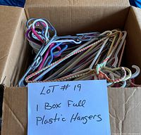 Box of assorted plastic hangers in multiple colors and styles, some wrapped with fabric.