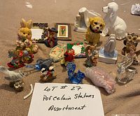 Wide assortment of 18 porcelain and glass figurines including animals, human figures, flowers, decorative plaques, and picture frames placed on carpeted floor.