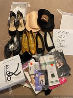 Photo showing a collection of women's shoes alongside unopened packages of spandex pantyhose and foot display pieces on carpeted floor. A handwritten note states lot number and contents.