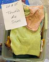 Plastic bin filled with assorted towels of varying sizes and colors, including light green, peach, yellow and dark green colors.