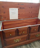 Wood chest with open hinged lid, showing internal storage and multiple drawers beneath.