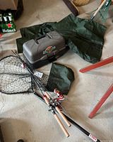Photo showing three fishing rods with Abu Garcia Specialist red spinning reels, green waders, green jacket, black fishing net, and grey Flambeau tackle box on the floor.