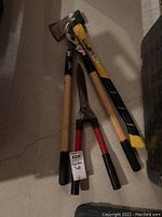 Garden tools laid on concrete floor: small axe, hedge shears, pruning shears
