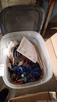 Top view showing contents of bin including white rope, blue ratchet straps, propane heater parts and manual.