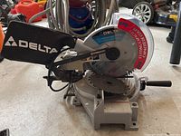 Side view of Delta miter saw showing blade, dust collection bag with Delta logo and base with angle adjustment.