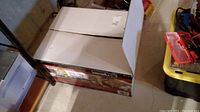 Boxed Nexgrill portable stainless steel gas grill in basement setting with nearby tools and storage containers.