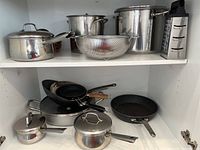 Full view of cookware set including pots with lids, strainer, pans, and box grater arranged on two shelves