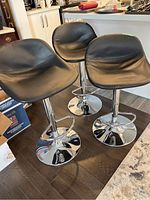 Three black adjustable bar stools with padded seats and chrome bases arranged in a kitchen area.