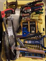 Photo showing assortment of hand tools including hammers, a saw, screwdrivers, wrench set, and levels in a yellow plastic bin.