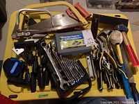 Overview of all tools laid out on yellow plastic tray including saws, hammers, pliers, wrenches, screwdrivers, tape measure, and screw extractor set.
