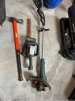 Full lot view showing three items: axe, hedge trimmer, and trimmer on concrete floor.