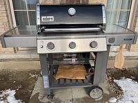 Front view of Weber Genesis II GS4 barbecue grill showing three control knobs and lower storage shelf