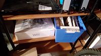 Photo of Nintendo Wii console box and blue plastic bin with games and accessories below desk.