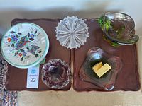 Five ashtrays displayed on a wooden surface with two gold-tone lighters in one ashtray.
