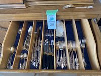Wooden drawer insert filled with assorted silver plated cutlery including forks, spoons, and knives with black handles.