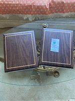 Two closed hardcover albums with wood-effect and gold border design placed on glass table.