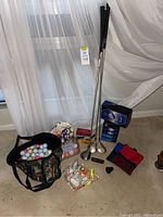 Overall view of golf clubs, bags, golf balls, tees, and accessories arranged on floor in front of a window with curtains.