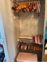 Photo of closet corner with natural cedar wood hangers hanging on rod on top and various cloth and wooden hangers hanging on rod below, with pink and white wicker hamper below
