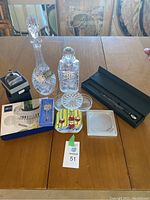 All items arranged on wooden table including decanters, boxed Mikasa wine set, decorative plates, glass dishes and ice tongs.