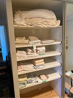 Shelving unit with stacked linens including bedspreads and towels