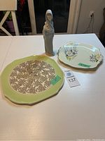 Full view of Lladro unglazed woman figurine with two vintage decorative plates on a white table