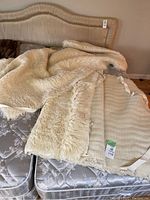 Two vintage sheepskin bed covers laid on a bed mattress, showing the fleecy texture and fabric edging with ties.
