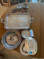 Photo showing the full collection of silver plated serving ware on a wooden table, including trays, plates, small containers, and a covered dish.