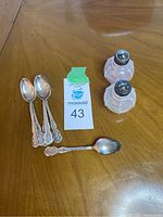 Photo showing six small sterling silver spoons alongside two glass salt and pepper shakers with silver tops.