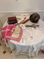 Overview of vintage baking items on round table, showing aprons, rolling pins, egg beater, cake pan, and two recipe books